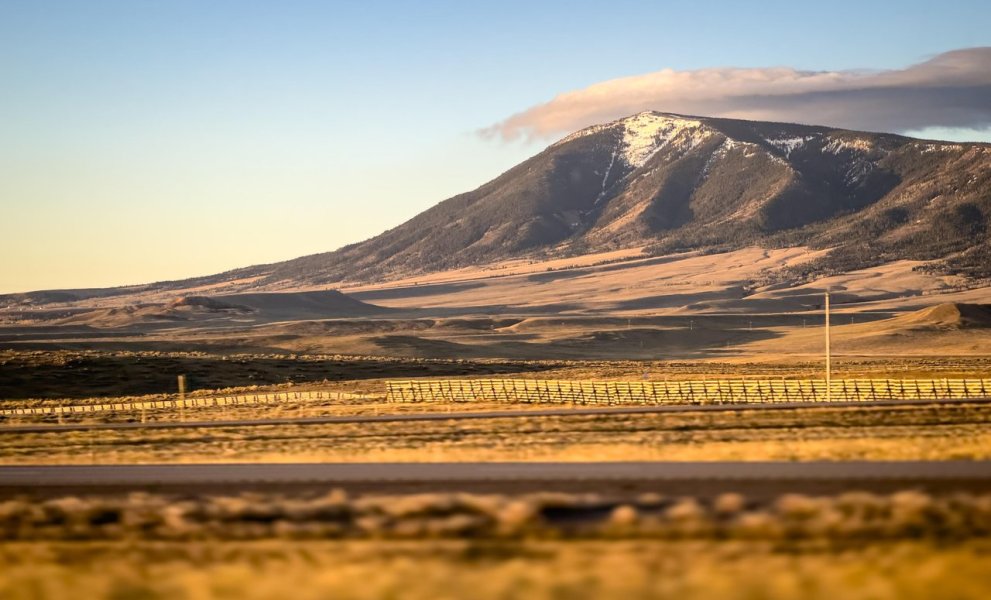 A sprawling golden landscape with snow-dusted Elk Mountain, its peak touching gray clouds.
