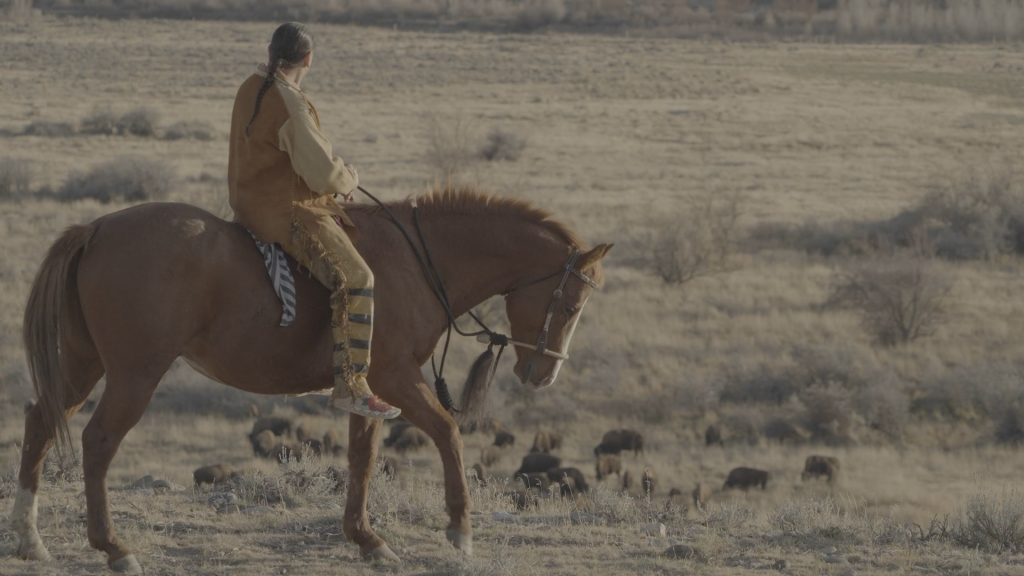 A native american rides a horse across the prairie.