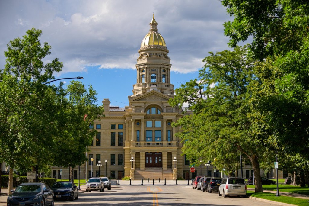 8 Historic Landmarks & Sites In Wyoming 2 A street lined with parked cars and rows of trees, and in the background, the Wyoming State Capitol.