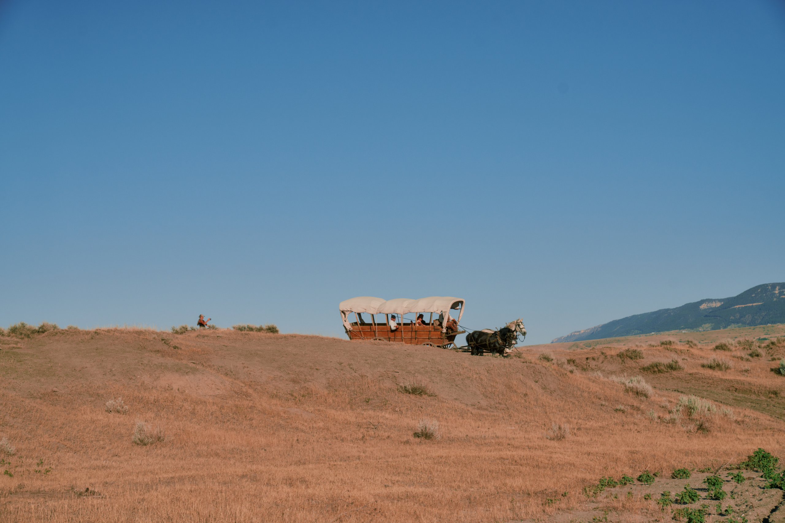 Tracing the Past: 6 Historic Trails In Wyoming 1 Travelers ride in a covered wagon drawn by horses across Wyoming’s rugged landscape, with mountain views on the horizon.