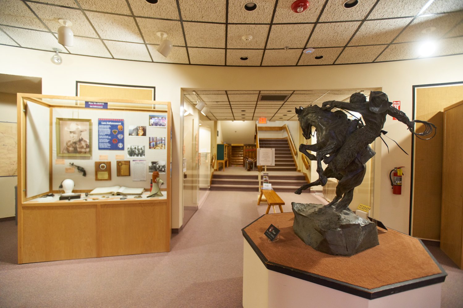 A museum exhibit features glass-encased memorabilia and a sculpture of a cowboy on horseback mid-air.