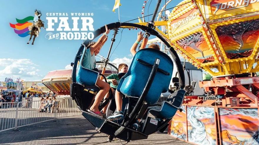 Central Wyoming Fair and Rodeo logo in the sky above kids on a carnival ride with their hands raised in excitement.