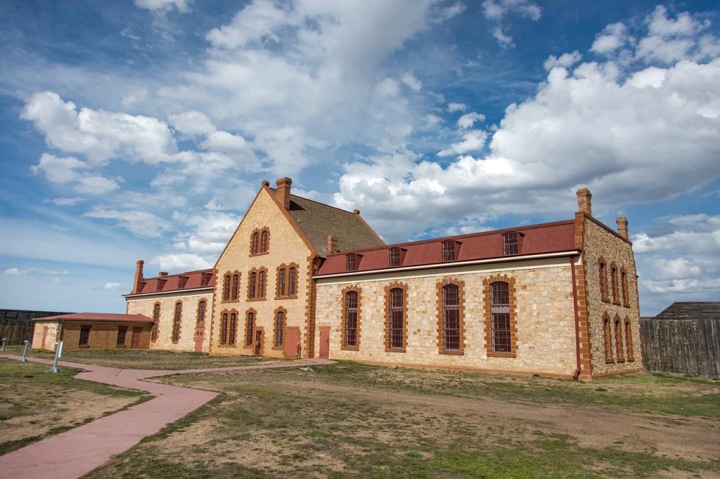 8 Historic Landmarks & Sites In Wyoming 4 A wide shot of the Wyoming Territorial Prison State Historic Site, surrounded by a field of grass and dirt.